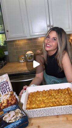 a woman sitting at a kitchen counter holding a large casserole in front of her