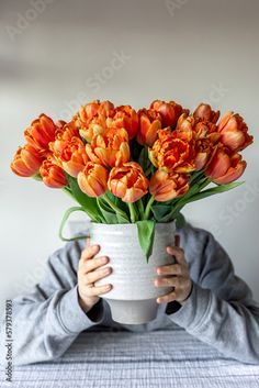 a person holding a white vase with orange tulips in it's mouth