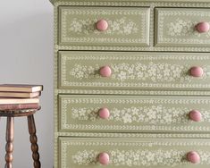 a green dresser with pink knobs on it next to a small table and chair