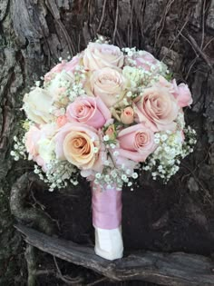 a bridal bouquet with pink roses and baby's breath in front of a tree