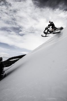 a man riding a snowboard down the side of a snow covered slope on a cloudy day