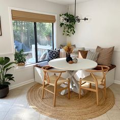 a dining room table with chairs and a bench in front of a window that has potted plants on it