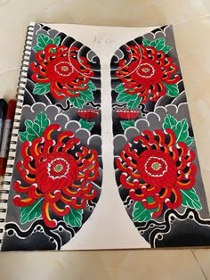 an open notebook with red and green flowers painted on it next to a marker pen