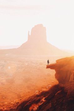 a lone person standing on top of a rocky cliff in the middle of desert land