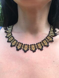 a woman wearing a black and gold beaded necklace with yellow beads on her chest