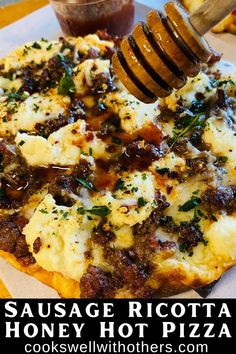 a pizza with cheese, meat and sauce on it is being held by a wooden spatula