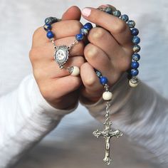 a person holding a rosary with a cross on the front and blue beads around it