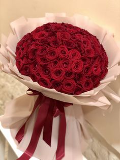 a large bouquet of red roses wrapped in white paper and tied around the top with ribbon