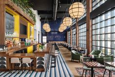 the interior of a restaurant with striped rugs and wooden bar stools, large windows, and hanging lights