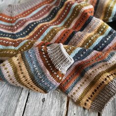 a multicolored knitted blanket laying on top of a wooden floor next to a black cat