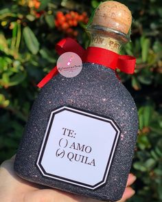 a hand holding a bottle of tequila with a red ribbon around its neck and label on it