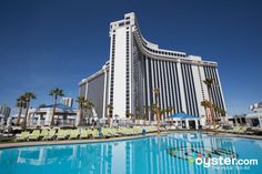 a large hotel building next to a swimming pool with lawn chairs and umbrellas around it