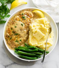 a white bowl filled with mashed potatoes and green beans next to a lemon wedge