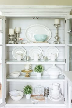 a white china cabinet filled with dishes and cups on top of it's shelves