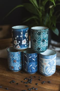 five blue and white cups sitting on top of a wooden table next to a potted plant