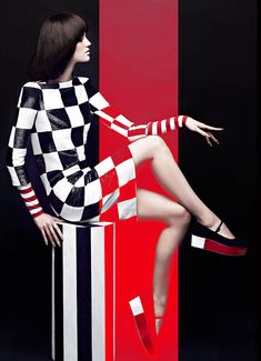 a woman sitting on top of a red and black striped box with her legs crossed