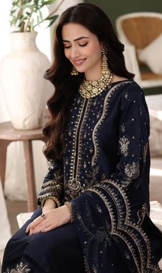 a woman sitting on top of a chair wearing a blue dress with gold accents and jewelry