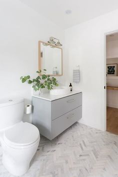 a white toilet sitting next to a sink in a bathroom under a mirror and a potted plant