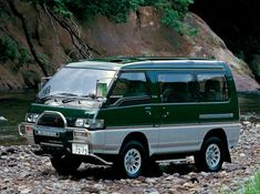 a green van parked on the side of a river next to some rocks and trees