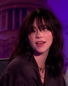 a close up of a person sitting in a chair with a purple light behind her