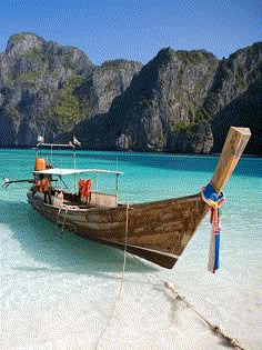 a boat is docked on the beach in front of some mountains and clear blue water