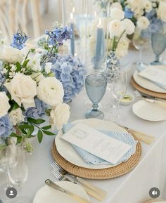 the table is set with blue and white flowers, silverware, and napkins