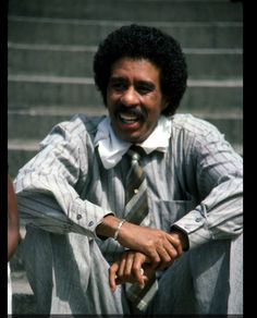 a man sitting on the steps with his hands folded out and wearing a striped tie