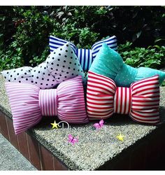 four different colored pillows sitting on top of a stone bench in front of some bushes