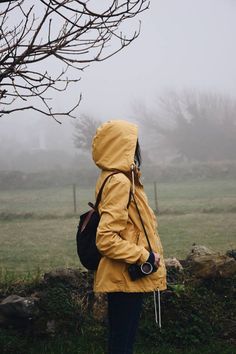 a person in a yellow jacket is standing by a tree and looking at the fog