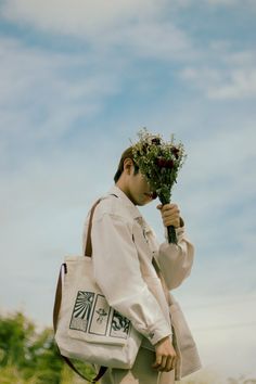 a woman carrying a white tote bag with flowers in her hand while walking through the grass