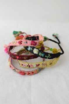 four bracelets with flowers and tassels sitting on a white tablecloth covered surface