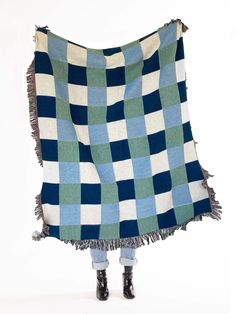 a woman is holding up a blue and green checkered blanket with fringes on it