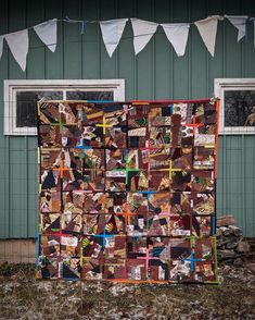 a quilt hanging on the side of a green building with buntings above it