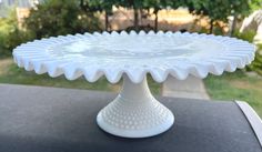 a white cake plate sitting on top of a table in front of some bushes and trees