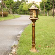 a lamp post in the middle of a grassy area next to a path and trees