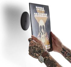 a person holding up a book in front of a white wall with tattoos on it