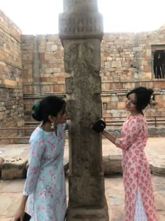 two women standing next to each other near a stone pillar