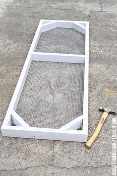 a hammer laying on the ground next to a window frame with mesh covering it and a wrench