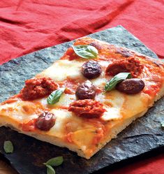 a piece of pizza with olives and cheese on it sitting on a red cloth