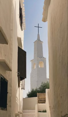 the steeple of a building with a cross on it is seen from between two buildings