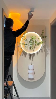 a woman is painting a vase with flowers in it on the wall next to a ladder