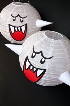 two white paper lanterns with faces and horns on them, one has red eyes and the other has large teeth