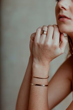 a woman with her hand on her chin wearing a gold bracelet and ring, looking off to the side