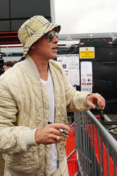 a man in a hat and jacket standing next to a metal fence holding a cell phone