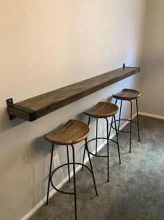 three wooden stools sitting next to each other in front of a wall mounted shelf