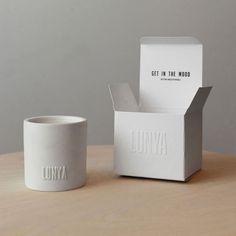 a white coffee cup sitting on top of a wooden table next to a cardboard box