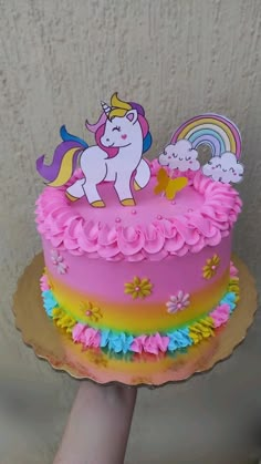 a hand holding up a cake decorated with pink frosting and rainbows on it