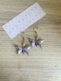 two origami butterflies are hanging from gold earwires on a wooden table