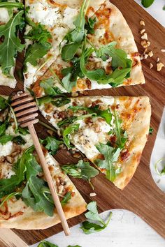 a pizza with spinach and cheese on it is cut into four slices, sitting on a cutting board