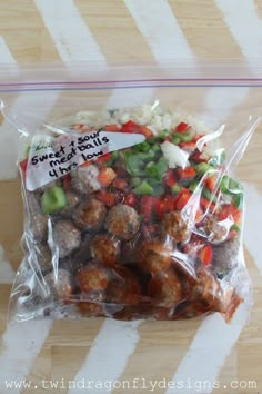 a plastic bag filled with meatballs and veggies on top of a wooden table